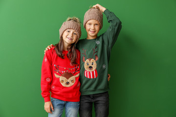 Little children in Christmas sweaters and knitted hats on color background