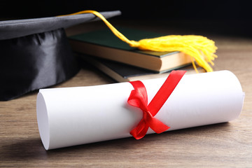 Graduation hat, books and student's diploma on wooden table