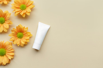 White cosmetic tube and yellow flower heads on a light background. Cosmetic mock up.