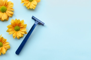 Blue disposable shaver and yellow flower heads on a blue background. Shaving and skin care for men concept.