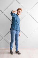 Portrait of young man pointing at viewer near grey wall