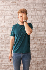 Portrait of young man covering eye with hand on brick background