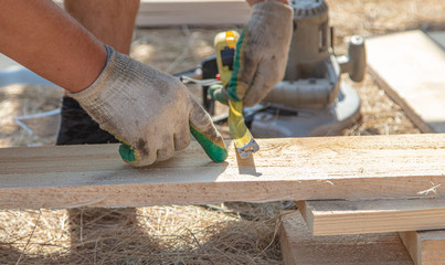 Worker measures a wooden board at a construction site