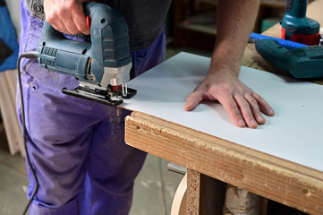 The worker makes, assembles a furniture cabinet from parts. Showing tools for work. The photo was taken in a really working manufactory.