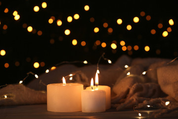Burning candles and Christmas lights on table against dark background