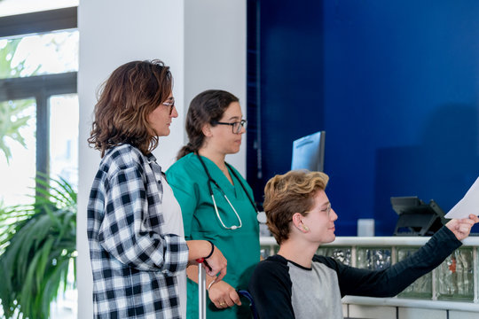 A lady and a nurse accompanying a blond boy to deliver a document, in the lobby of a clinic.