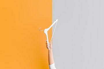 Female hand with clothes hanger on color background