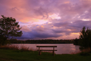 Romantic sunset over the water. Bench in foreground. Rural scene with dramatic sky. 