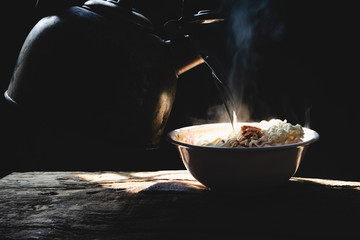 Steam and smoke Instant noodles in bowl on wooden table and nature light and black background,...