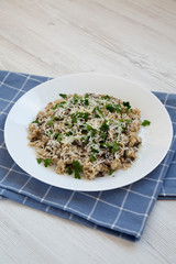 Homemade mushroom risotto with parsley on a white plate on a white wooden surface, low angle view.