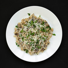 Homemade mushroom risotto on a white plate over black background, top view. Flat lay, overhead, from above.