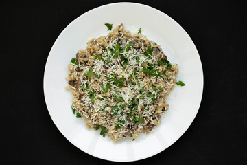Homemade mushroom risotto on a white plate on a black surface, top view. Flat lay, overhead, from above. Close-up.