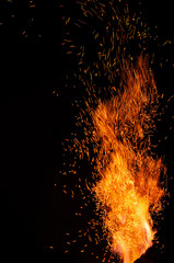 Flame of fire with flying burning red sparks on a black background. Fiery orange glowing particles...