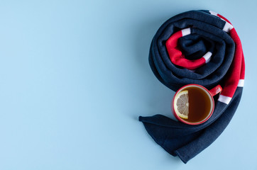 Cotton colored scarf with tea cup and lemon slice composition on blue background.