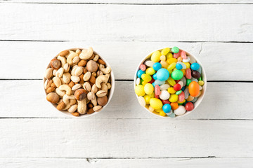 Diet decision concept. Mixed nuts and sweet in bowls on white wooden background. Top view