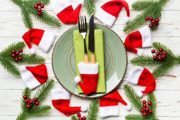 Holiday composition of plate and flatware decorated with Santa hat on wooden background. Top view of Christmas decorations. Festive time concept