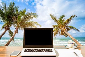 Mockup of laptop computer with empty screen with smartphone and coffee cup on wooden on table at landscape early sunrise over blue the sea background,working on the beach,Freelance work and holiday