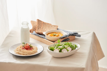 Breakfast table; spaghetti served with radish and salad with pumpkin puree, bread, milk set on table