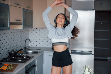 Dancing to the music. Girl in the modern kitchen at home at her weekend in the morning time