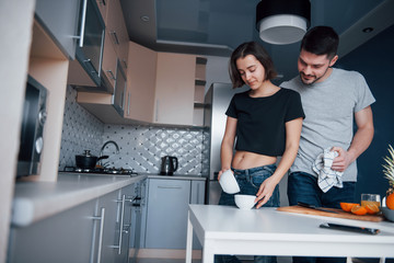 Obraz premium Pouring the water. Young couple in the modern kitchen at home at their weekend in the morning time