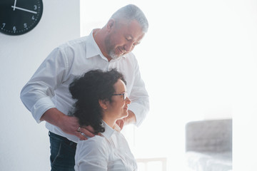 Making massage for relaxation. Senior man and his wife in white shirt have romantic dinner on the kitchen