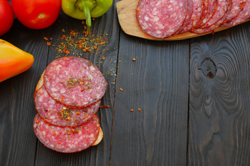Homemade fast food. Making sandwich. Sliced salami and ripe vegetables lie on dark wooden table. For the preparation of sandwich with sausage. On dark wooden background.