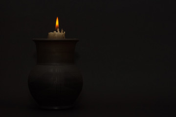 Burning candle in a black ceramic pot on a dark background. Concept of divination, magic, ritual. Copy space.