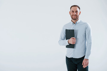 Black notepad in hands. Man in official clothes stands against white background in the studio