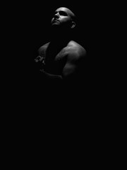 Obraz na płótnie Canvas Low key black and white photo of a hairy chested man flexing his left arm while looking towards the light
