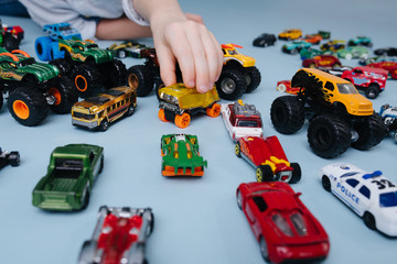 Boy's hand playing with, moving one toy model car of many on the floor over blue