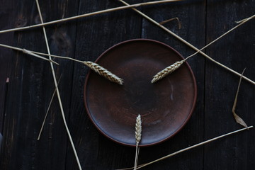 three wheat spikelets on a clay plate on a black burnt