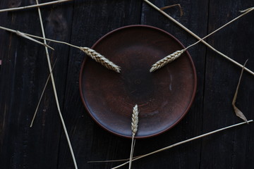 three wheat spikelets on a clay plate on a black burnt