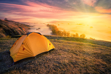 Orange tent on hill above foggy river under bright sun © alexlukin