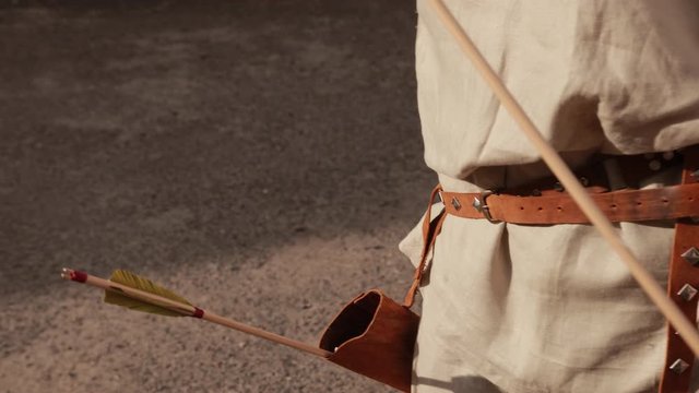 archery. man in gray linen suit with brown belt with metal inserts, pulls arrows from special bag for bow, close-up, slow motion