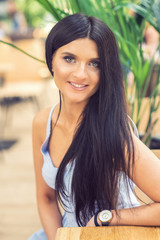 Beautiful young brunette woman in blue dress against of summer background. Closeup portrait of beautiful young smiling woman with long hair outdoors.