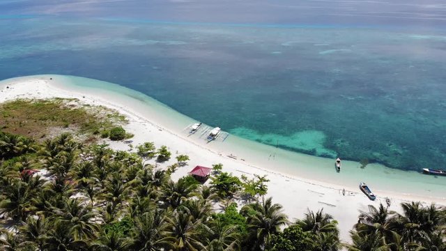 4K aerial rising shot of secluded beach and boats looking over clear blue water in Balabac, Palawan Philippines