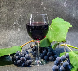 Grapes in a glass with wine on a black background. Grones of grapes with green leaves..