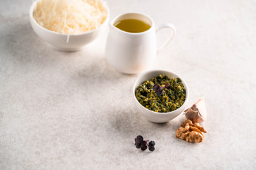 pesto sauce in a white bowl, on a marble backdrop, olive oil and cheese bowl on the background