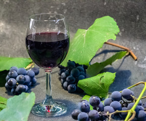 Grapes in a glass with wine on a black background. Grones of grapes with green leaves..