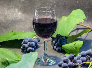 Grapes in a glass with wine on a black background. Grones of grapes with green leaves..