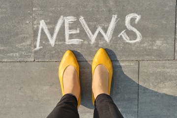 Word news on gray sidewalk with women legs, top view