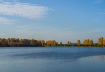 Beautiful blue lake with clear sky. Autumn yellow forest in the distance on the horizon.