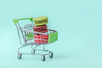Assorted colorful macaroons in toy shopping cart on mint green background with copy space.