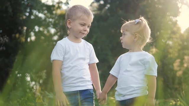 Happy family: little boy a and girl brother and sister hold hand on nature happy children concept. children look into the distance slow motion video. lifestyle childhood kids play