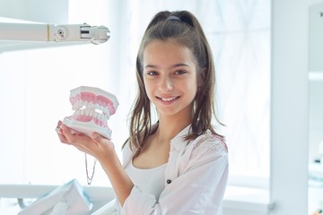 Smiling teenager girl in dental office holding jaw model with teeth