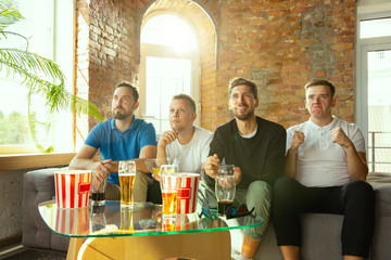 Group of friends watching game on TV at home. Sport fans spending time and having fun together. Emotional, expressive, exciting game. Cheer for favorite football or soccer team, friendship, weekend.