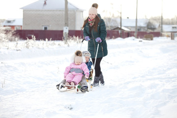 Fototapeta na wymiar Happy young woman with two children on a sled on winter walk