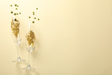 Champagne glasses with glitter on beige background, space for text