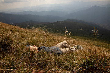 Tourist girl resting in the mountains. Tourist girl lying on the grass in the mountains. Stylish traveler woman lying on grass and relaxing in mountains. Travel concept.
