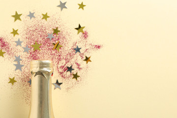 Champagne bottle and glitter on beige background, close up